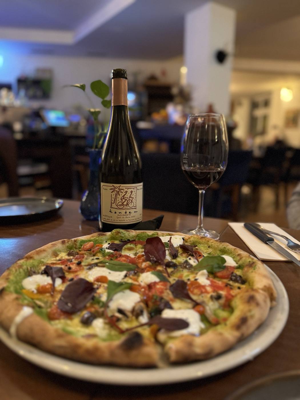 Pizza mit Pesto, Kirschtomaten und Burrata und ein Glas Rotwein im Gastraum von AnaMiRa
