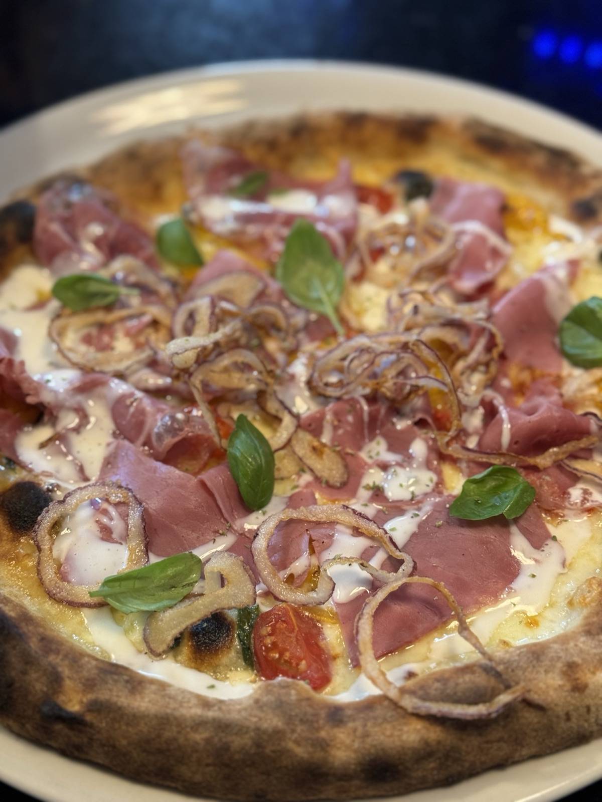 Pizza with pastrami, roasted onions, cherry tomatoes and basil